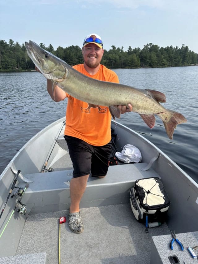 Man holding a muskie in a boat.